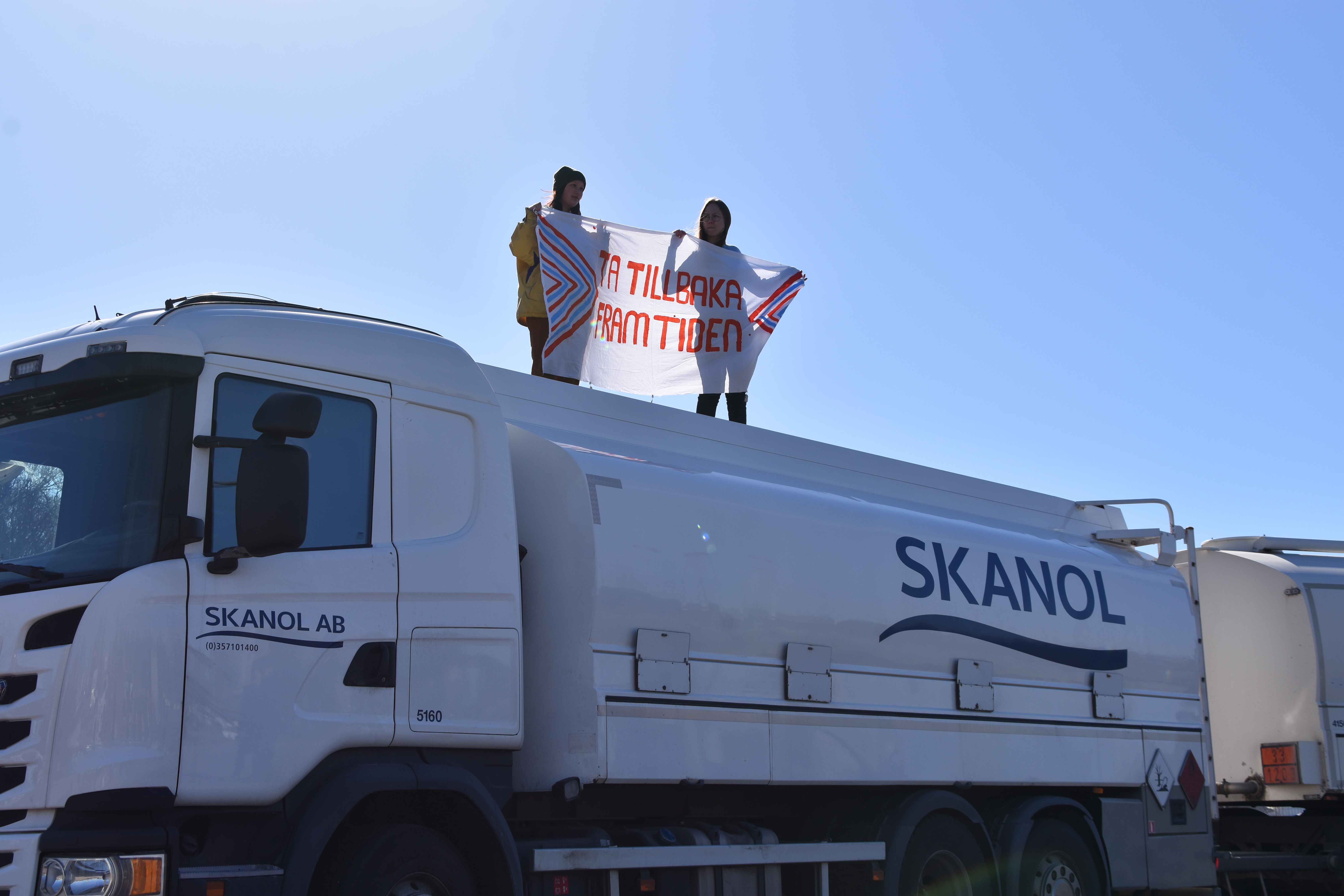 Två aktivister med en &ldquo;Ta Tillbaka Framtiden&rdquo;-banderoll på en vit tankbil